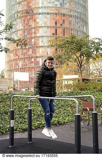 Young guy joining parallel bars outdoors while looking camera outdoors