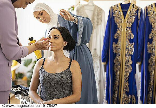 Young hairdresser with make-up artist preparing bride for wedding