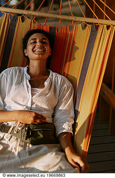 Young happy woman lying on a colored striped hammock.