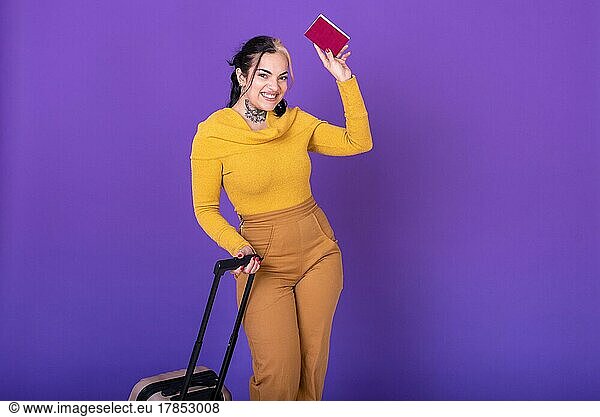 Young happy woman traveler with suitcase while showing her passport against purple background. Copy space