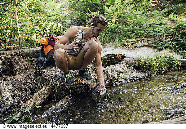 Young hiker scooping fresh water in a forest