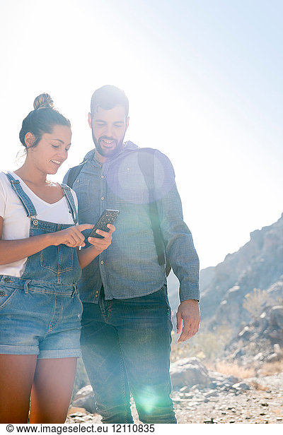 Young hiking couple looking at smartphone in sunlit valley  Las Palmas  Canary Islands  Spain