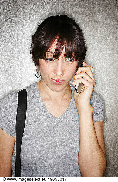 Young hip woman wearing suspenders on a cell phone with a quirky expression on her face.
