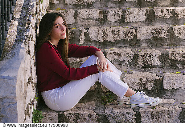 Young Hispanic teenage girl sitting on stone stairs looking drea