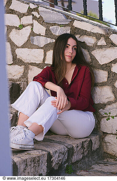 Young Hispanic teenage girl sitting on stone stairs looking drea