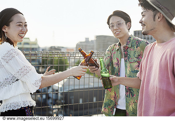 Young Japanese men and woman standing on a rooftop in an urban setting  drinking beer.
