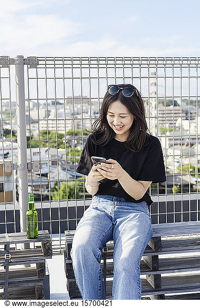 Young Japanese woman sitting on a rooftop in an urban setting  using mobile phone.