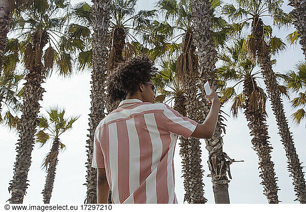 Young latin man with afro hair taking a selfie among palm trees