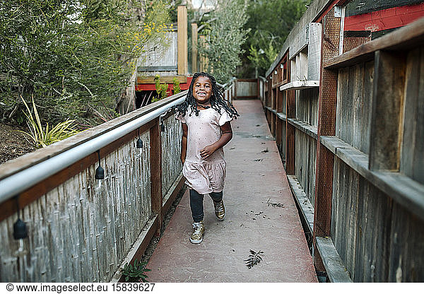 Young laughing black girl with long braids walking across foot bridge