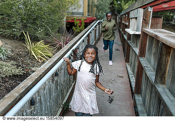 Young laughing black sisters running across wooden bridge