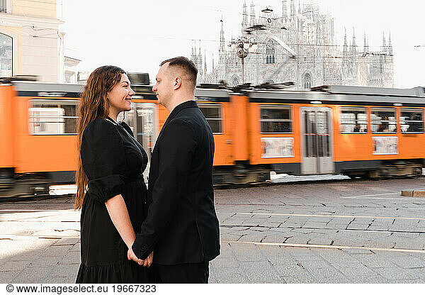 Young lovers stand in the center of Milan in front of a moving tram