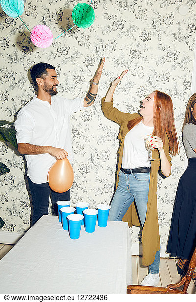 Young male and female friends giving high-five while standing by table during party at home