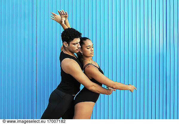 Young male and female gymnasts doing dancing pose by blue wall