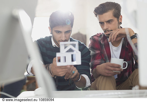 Young male architects examining house model