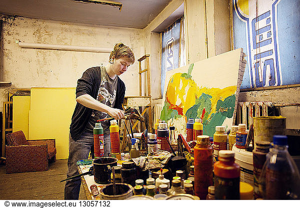 Young male artist painting standing by table at workshop