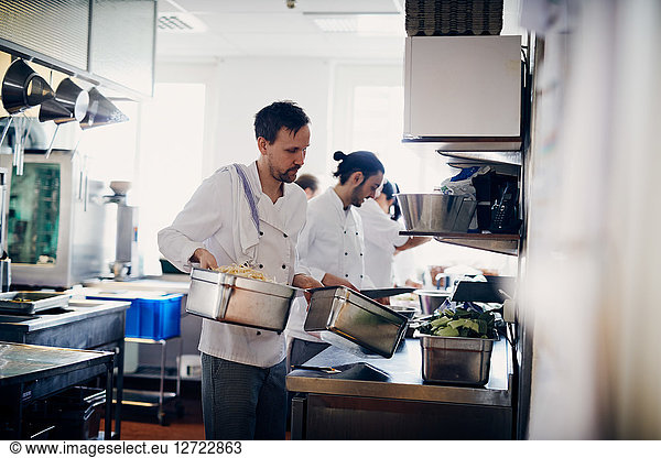 Young male chef carrying containers of food in commercial kitchen