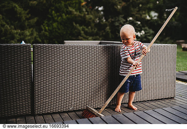 Young male child barefoot sweeping backyard patio with big broom