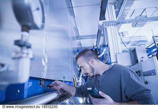 Young male engineer examining machine with multimeter in an industrial plant  Freiburg im Breisgau  Baden-Württemberg  Germany