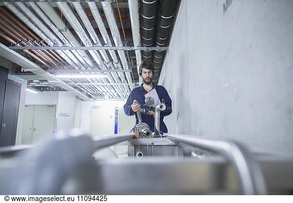 Young male engineer wearing headset and checking pipeline connection in an industrial plant