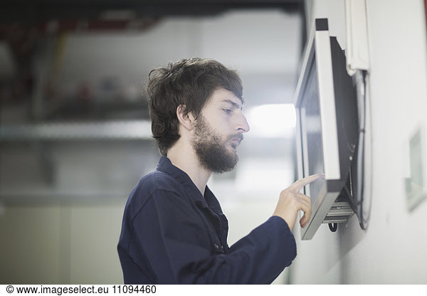 Young male engineer working on touchscreen computer monitor in an industrial plant