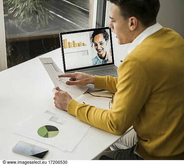 Young male entrepreneur discussing over document through video conference