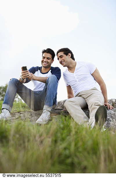 Young male friends sharing mobile phone outdoors