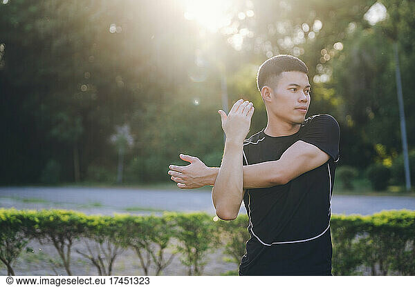 Young male jogger warming up by stretching arms and upper body b