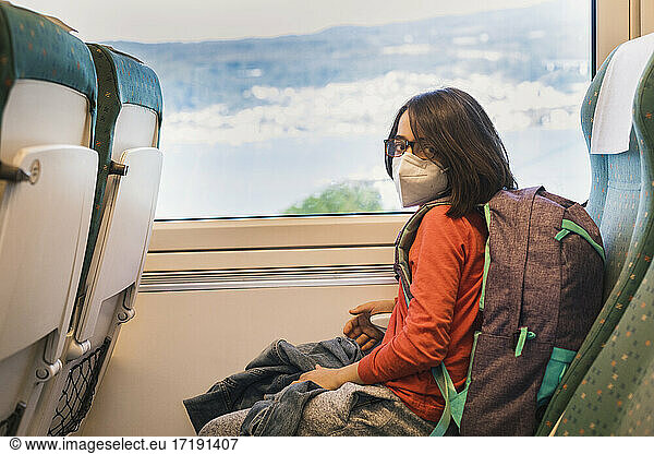 Young male looking camera wearing mask travels by train