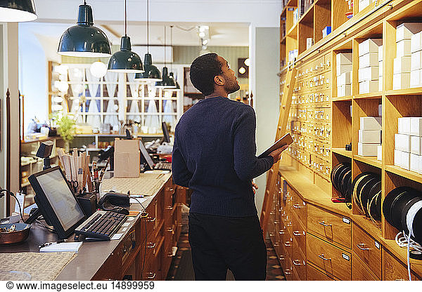 Young male owner looking up at boxes in furniture store
