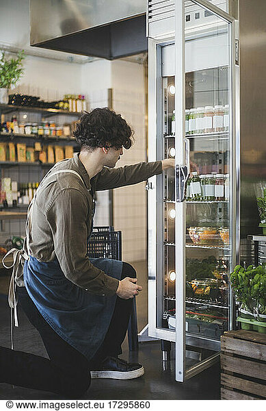 Young male owner taking bottle from refrigerator at store