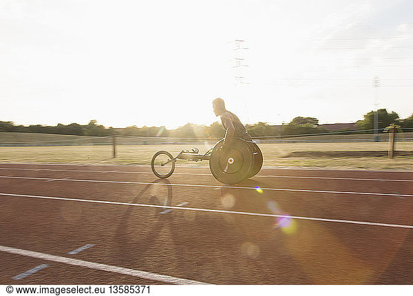 Young male paraplegic athlete training for wheelchair race on sunny sports track