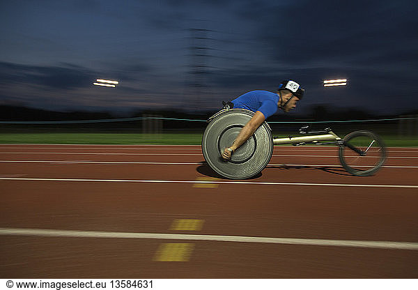 Young male paraplegic speeding along sports track during wheelchair race at night