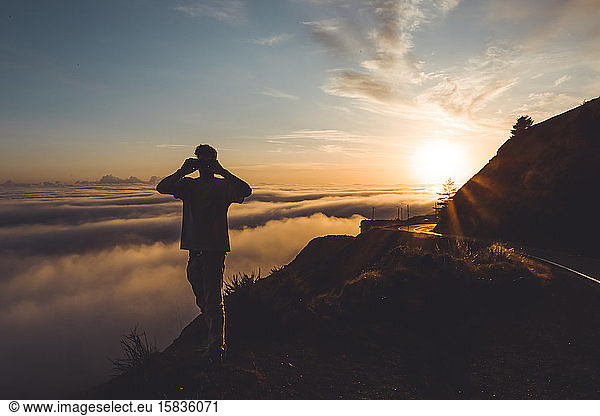 Young Male photographing sunset above clouds next to highway