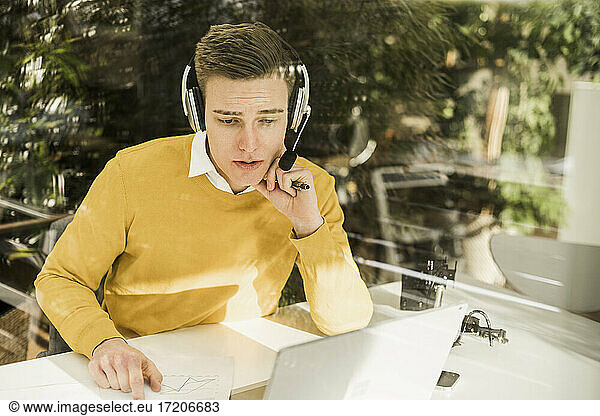 Young male professional wearing headphones attending business meeting in home office