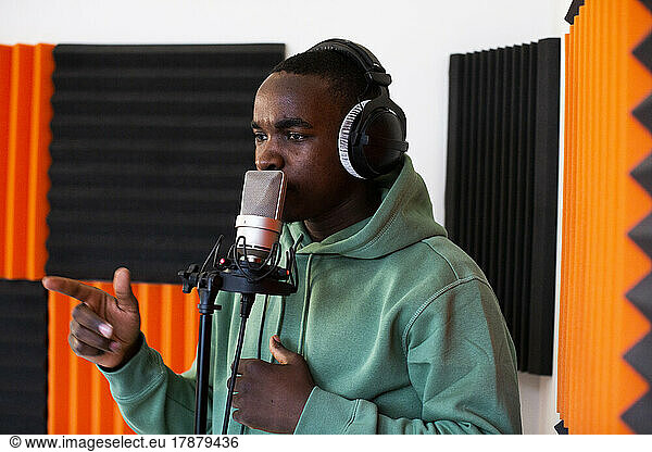 Young male rapper rapping on microphone while recording song in studio