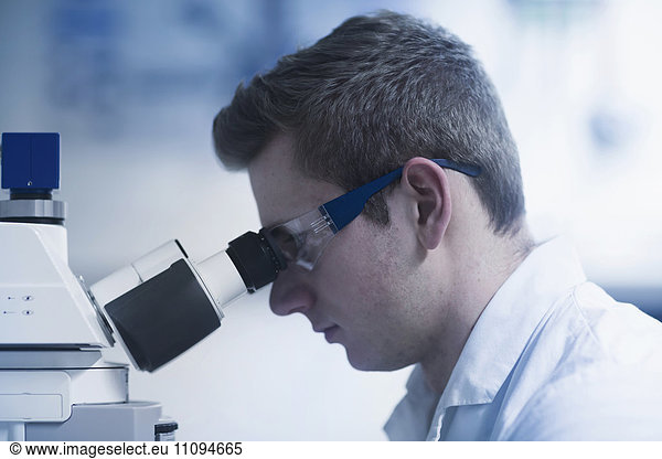 Young male scientist looking through microscope in an optical laboratory