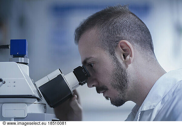 Young male scientist looking through microscope in an optical laboratory  Freiburg im Breisgau  Baden-Württemberg  Germany