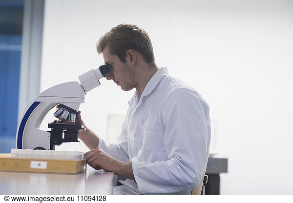 Young male scientist looking through microscope in lecture room