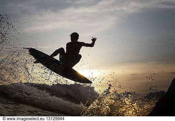 Young male surfer jumping over sea during sunset
