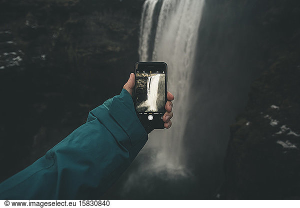 Young male taking a picture of waterfall with his smartphone