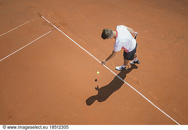 Young male tennis player preparing to serve the ball on sunny red tennis court  Bavaria  Germany