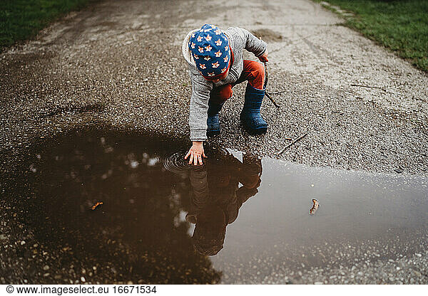 Young male toddler putting hand in a puddle at the park on cloudy day