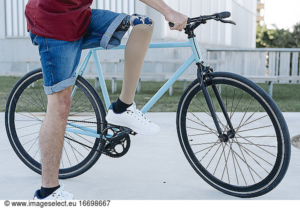 Young male with disability and prosthetic leg riding bicycle on street