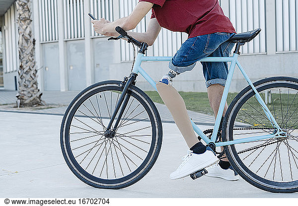 Young male with leg prosthesis sitting on bike and messaging