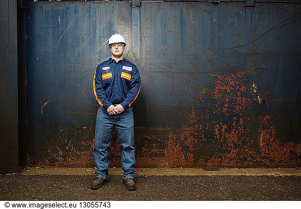 Young male worker standing against metal wall at recycling plant