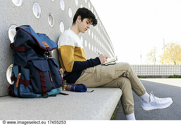 Young male writing notes in a notebook sitting on a bench