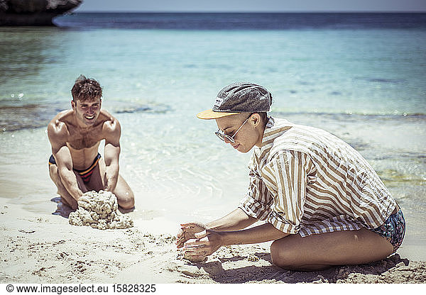 young man and woman build sand castles on pristine blue beach in sun