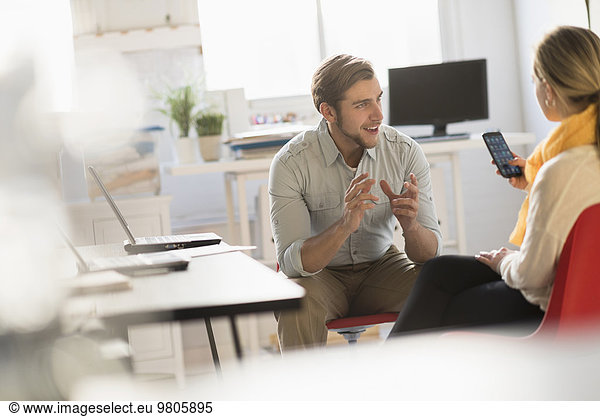 Young man and woman discussing at desk in office