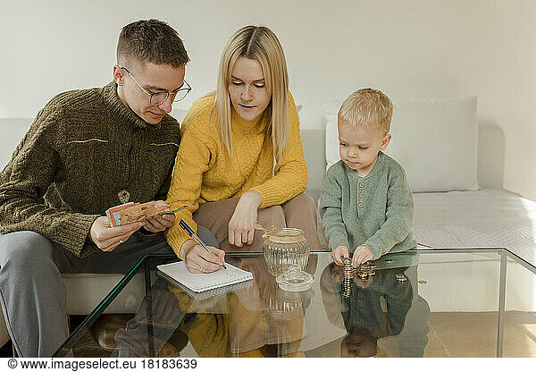 Young man and woman with son counting currency on table at home