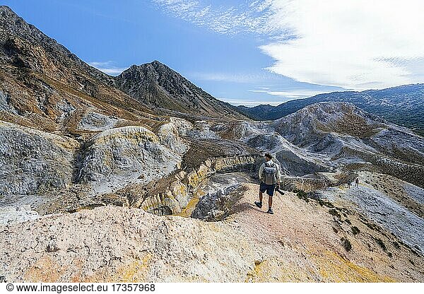 Young man at the crater rim  crater with yellow discoloured sulphur stones and colourful mineral deposits  volcano caldera with pumice fields  Alexandros crater  Nisyros  Dodecanese  Greece  Europe